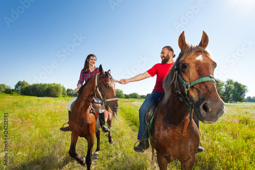 Happy young couple riding bay horses holding hands