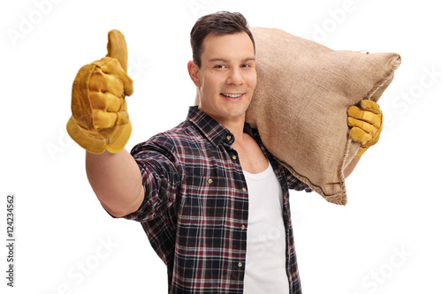 Male farmer holding burlap sack and giving thumb up