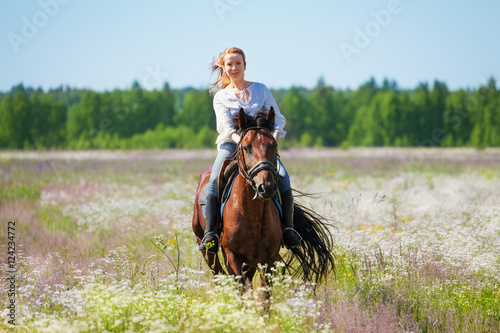 Young woman galloping horseback in flowery meadow