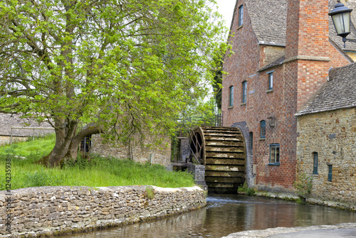 Old water mill with undershot waterwheel  and red brick chimney on the edge of traditional english village