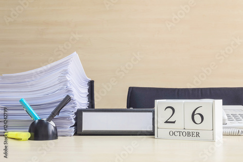 Closeup white wooden calendar with black 26 october word on blurred brown wood desk and wood wall textured background in office room view with copy space , selective focus at the calendar