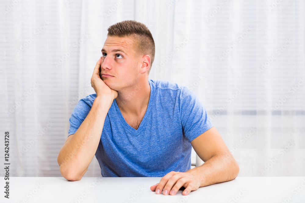 Depressed young man is sitting at the table and thinking about something.
