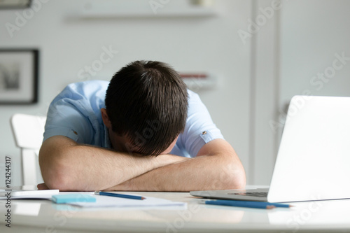 Fotografie Portrait of a man lying down at the desk near the laptop, head on his crossed hands, education, business concept photo