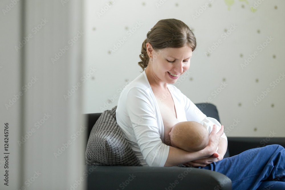 Fototapeta premium Portrait of a young attractive woman breastfeeding a child, holding on her knees. New born, bonding concept photo, view over the doorway, lifestyle