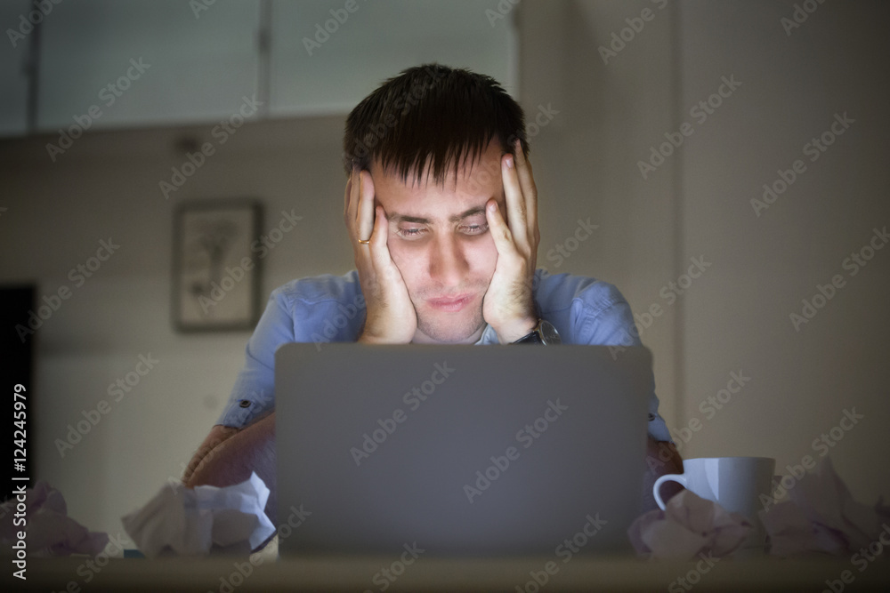 Φωτογραφία Portrait of a man grabbing his head in despair at the desk near the laptop, late at night