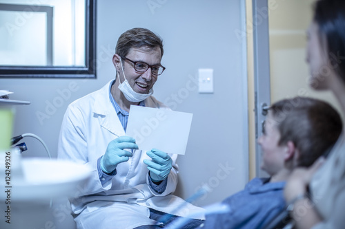 Smiling dentist holding paper with boy and mother in dental surgery