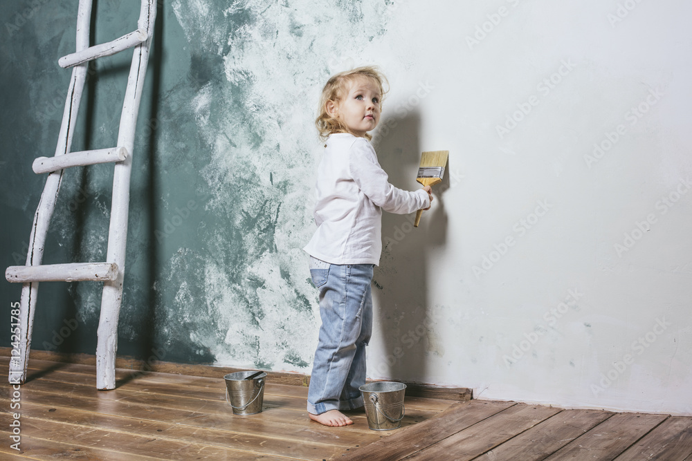 Little beautiful and happy child in jeans paint the wall with br Little beautiful and happy child in jeans paint the wall with br