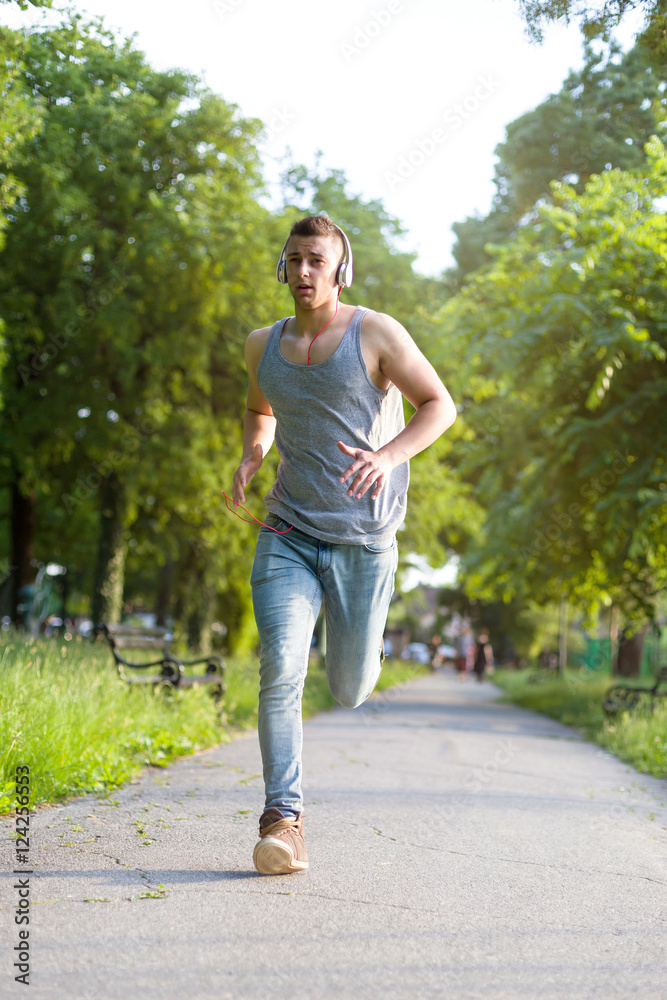Full length of handsome young man in sports clothing jogging in park. He is listening to music with his headphones Full length of handsome young man in sports clothing jogging in park. He is listening to music with his headphones
