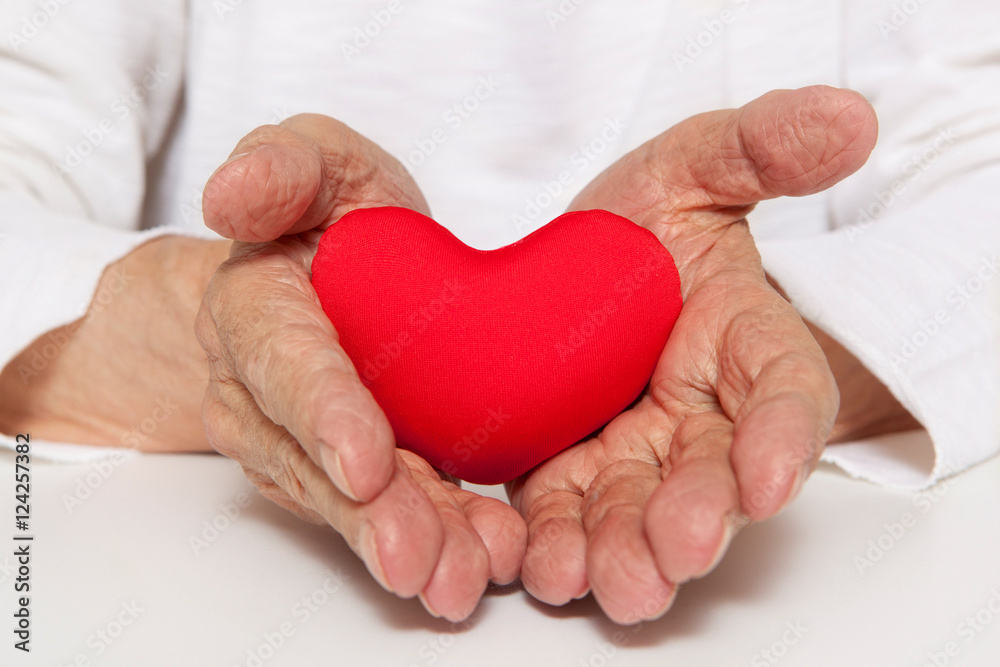 Old hands of the elderly giving a red heart