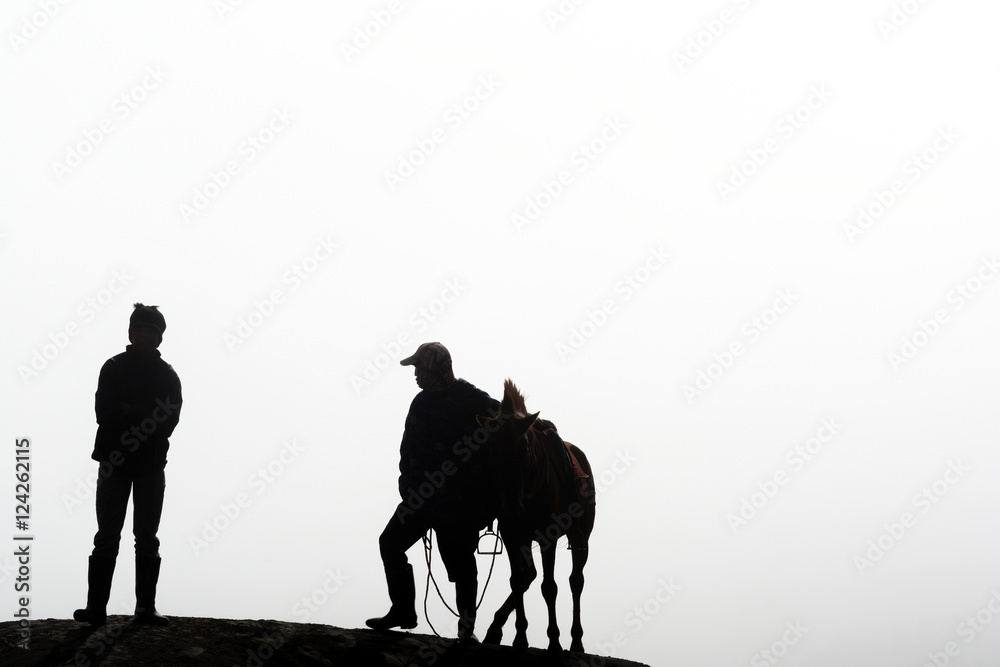Silhouette of two horsemen resting on the sand dune with foggy / misty morning background at Bromo-Tengger-Semeru National Park, East Java, Indonesia