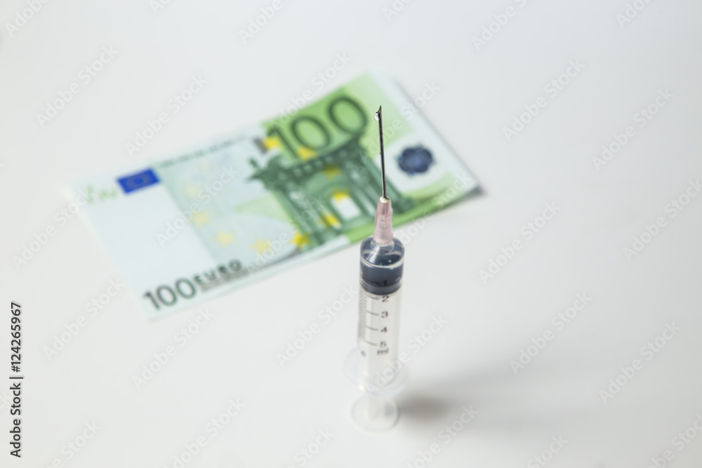 Syringe with needle and one hundred euro banknotes as a background with low focus. Syringe with needle and one hundred euro banknotes as a background with low focus.