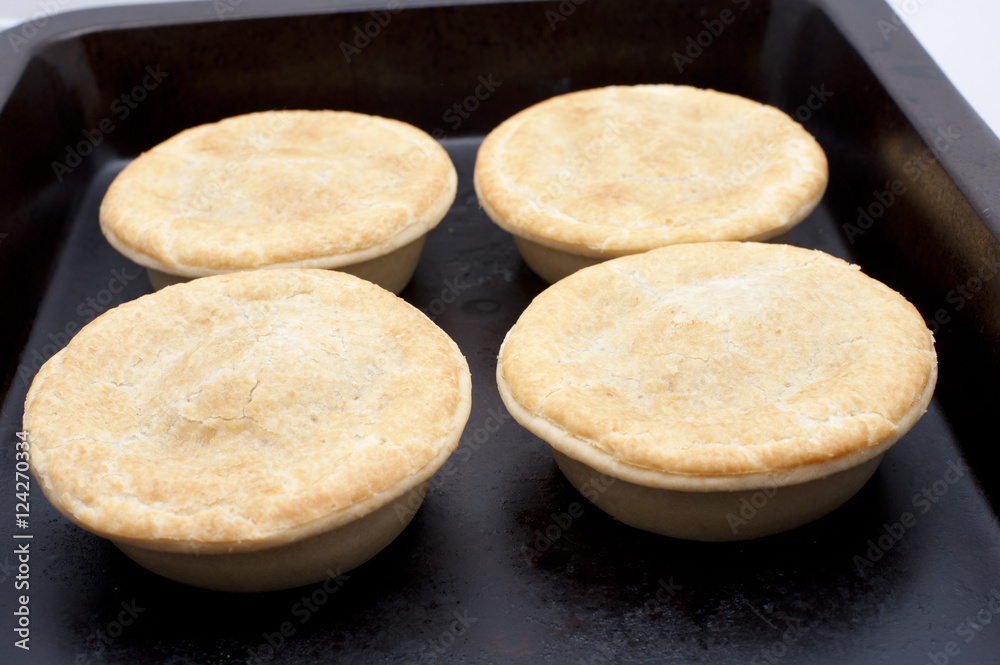 Four meat pies on a baking tray