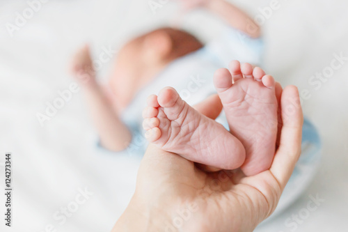 Mother holds newborn baby's bare heels. Tiny feet in woman's hand. Cozy morning at home. © Konstantin Aksenov
