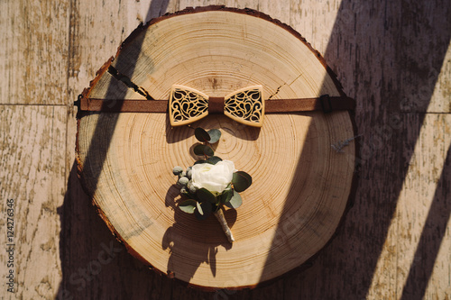 groom's wooden bow tie and boutonniere on round piece of wood in sunlight