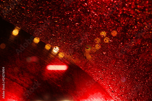 Raindrops on the windshield of the car, lit night lights.