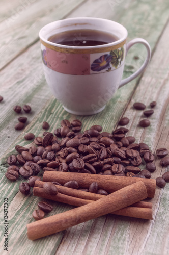 Cinnamon sticks on coffee beans with coffee cup on old rustic background