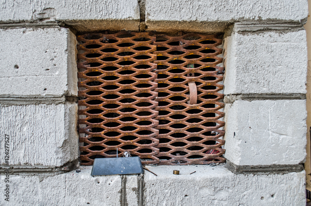 window in the basement with a grate of iron pipes / Small square secure window with bars on it. / close up of a window with metal grill / Metal barred or grated security installed on window