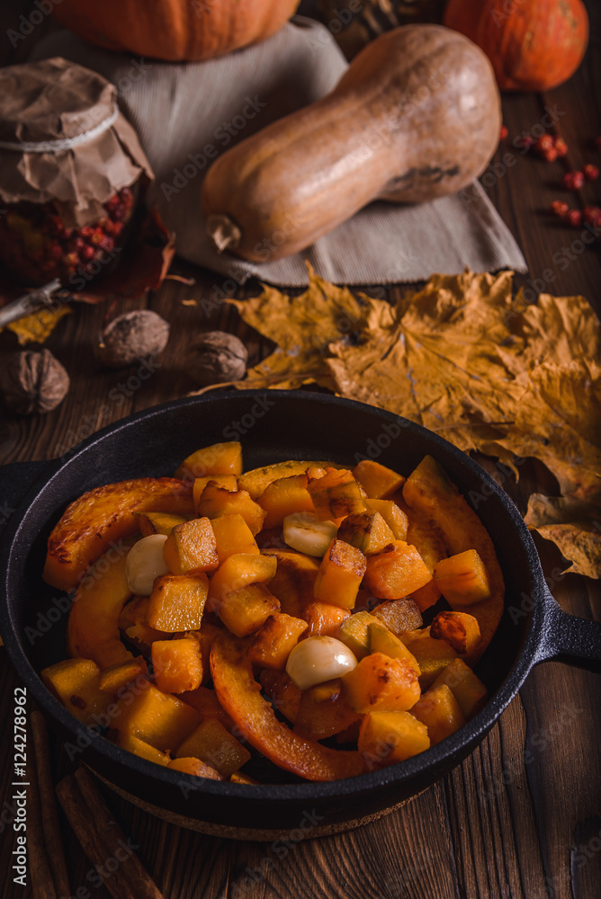 Autumn composition with pumpkin fried with garlic in a cast iron skillet on the old boards, with yellow maple leaves, walnuts and dried rose hips