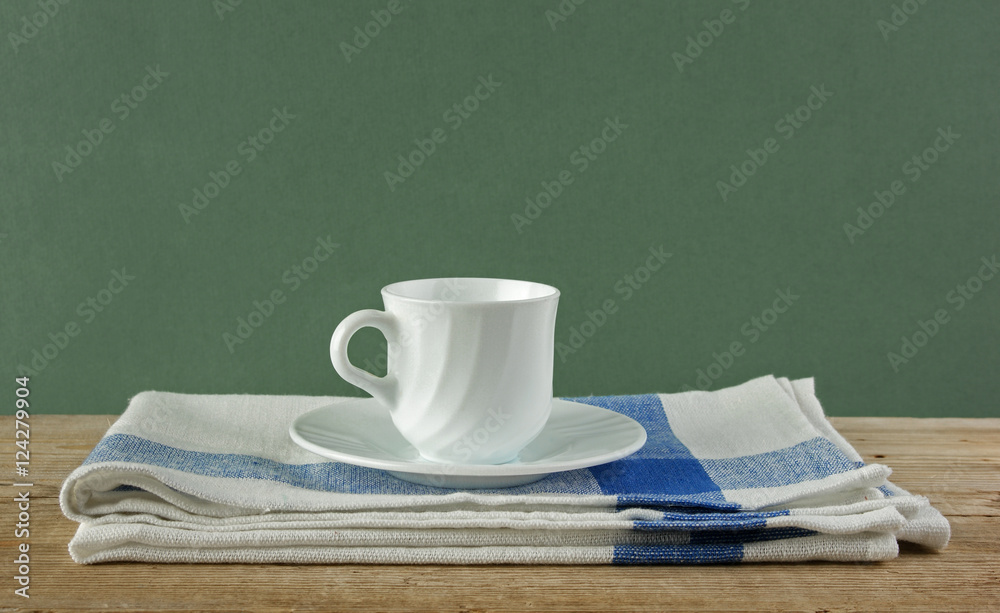 White coffee cup and dishcloth on old wooden table over green ba White coffee cup and dishcloth on old wooden table over green ba