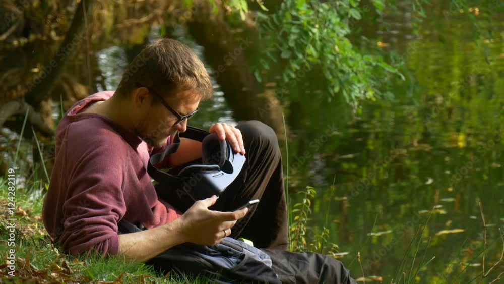 Young Man Holding 360Vr Glasses Clicks the Phone Park by the Water Tourist Looks Into the Glasses Watching Video 360 Degrees Playing Virtual Games Sunny Young Man Holding 360Vr Glasses Clicks the Phone Park by the Water Tourist Looks Into the Glasses Watching Video 360 Degrees Playing Virtual Games Sunny