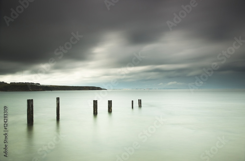 Wooden posts in a row in the shallow water along the coast under storm clouds;St. mary's bay northumberland england