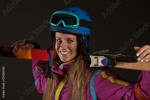 woman in ski costume posing with skis in studio on dark backgrou