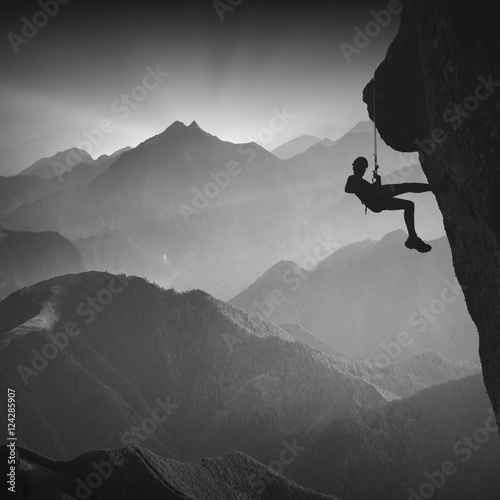Climber on a cliff against misty mountains. Monochrome