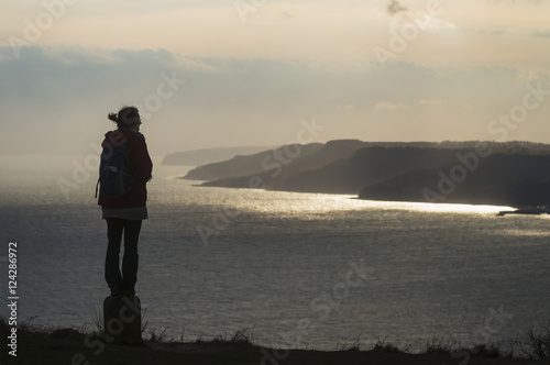 Silhouette of a woman admiring the view towards Lyme Regis from the top of Golden Cap on the Jurassic Coast; Seatown, Dorset, England photo