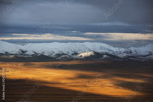 The late day sunshine illuminates the autumn coloured tundra along the Dempster Highway; Northwest Territories, Canada