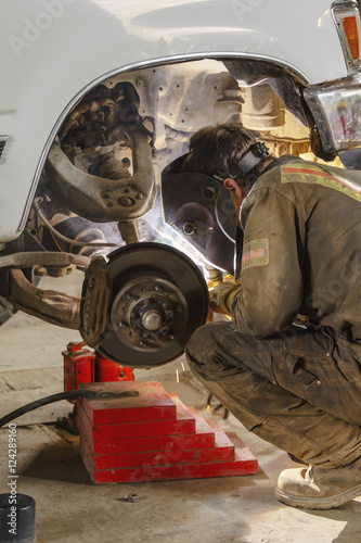 A welder wearing coveralls and his protective face shield is at work on a truck axle with a welding gun; Port McNeill, British Columbia, Canada