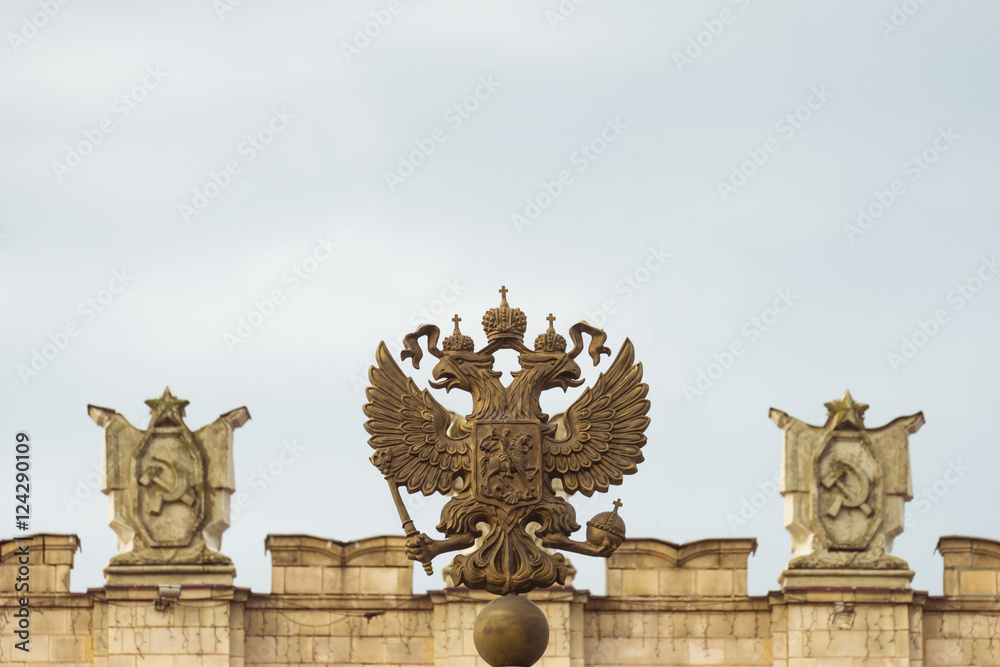 Coat of arms of the Russian Federation. Coat of arms  on the background of the parapet of the administrative government building with Soviet symbols. Free copy space at the top.