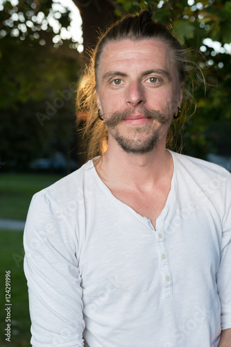 Portrait of man with long hair sitting outdoors in park while do