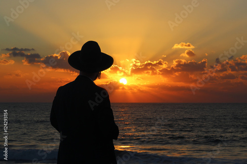 A religious Jew standing on the coast of Mediterranean sea and watching the sunset, deep in thought.