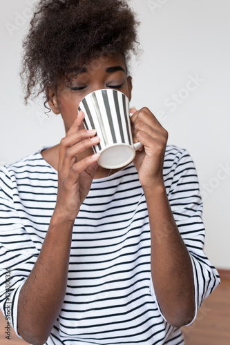 Beautiful african girl holding cup over light background.