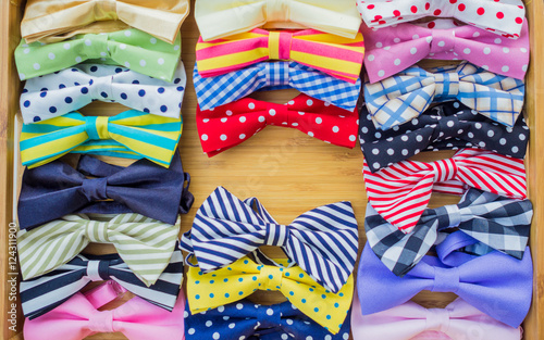 Collection of colorful bow ties with copy space in the middle on a wooden tray