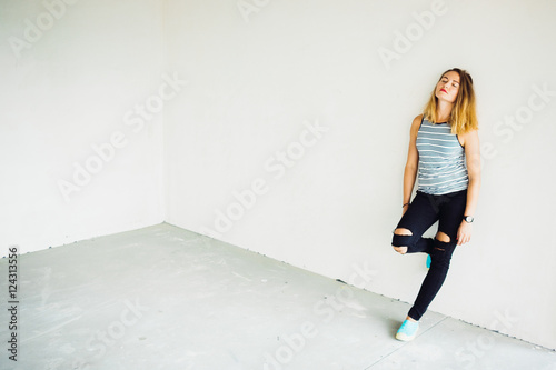 Thoughtful bronde wearing ripped black jeans leans on the wall
