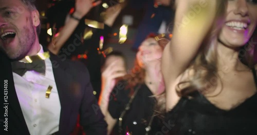 Shaky cam of tipsy gilded youth dancing in night club and laughing as two men in suits shooting confetti cannons over them 