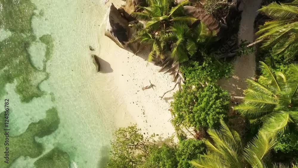 Aerial motion view of Seychelles tropical beach Anse Source D Argent at La Digue island with young woman sunbathing