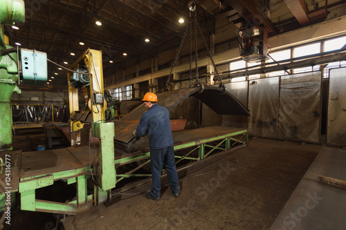 worker in factory at metal skip machine putting work piece in. metalworking and bending