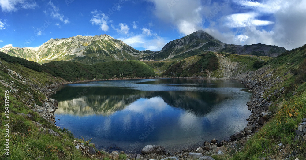 Panorama shot of Mount Tateyama mirrored in the Mikurigaike pond's cobalt blue surface at Murodo, Japan, as part of the Alpine Route. September, 2016.