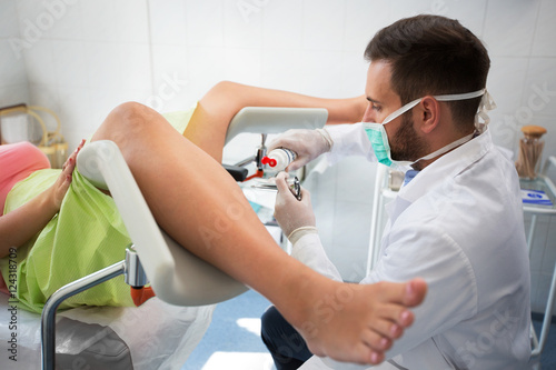 Foto Young gynecologist putting gel on equipment to exam patient