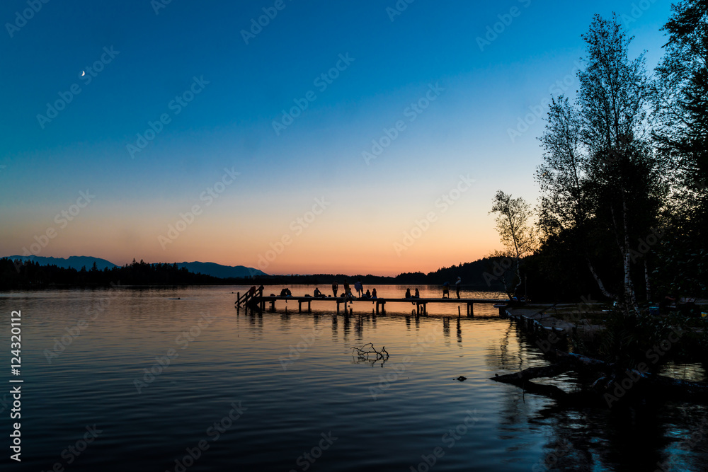 Kirchsee nahe Bad Tölz mit Badesteg, Badegästen und Alpenblick nach Sonnenuntergang