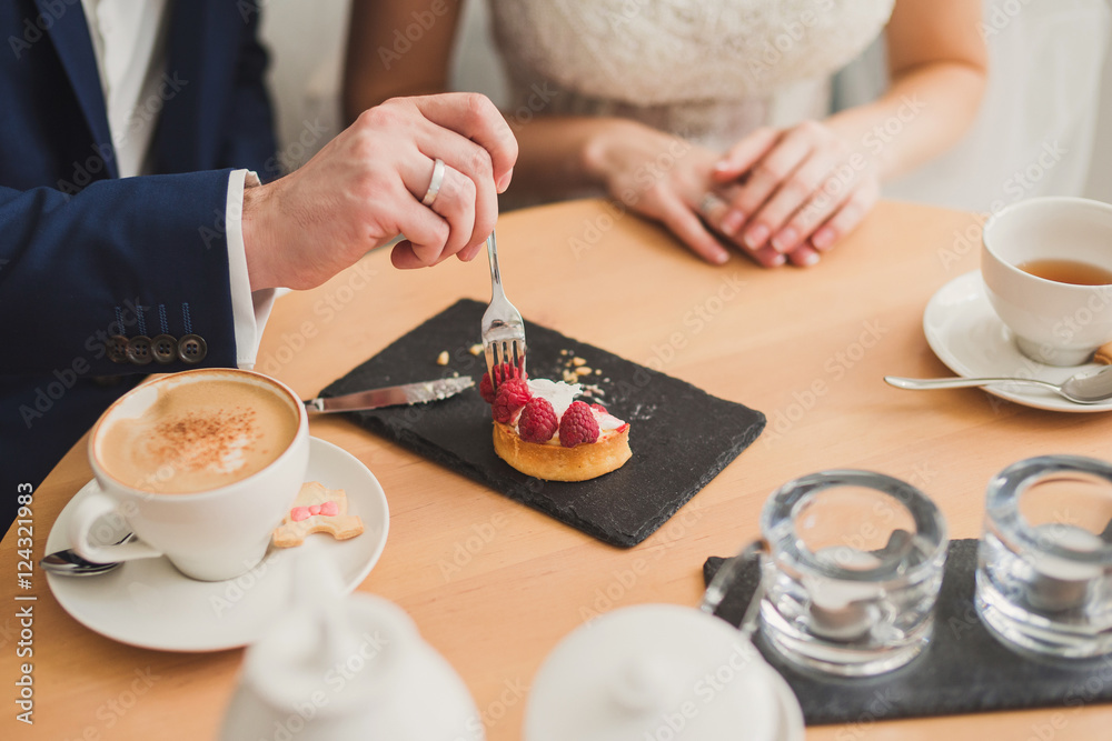 Closeup of bride and groom eating a sweet snack in cafe. Wedding rings on their fingers. Closeup of bride and groom eating a sweet snack in cafe. Wedding rings on their fingers.