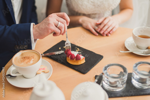 Closeup of bride and groom eating a sweet snack in cafe. Wedding rings on their fingers.