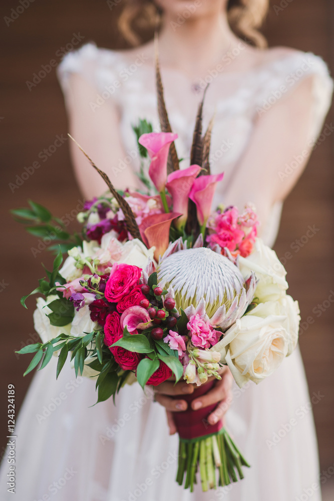 caucasian woman in beige wedding dress hold a bouquet of roses, berries and leaves with protea flower