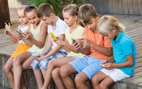 Group of smiling kids playing with mobile phones outdoors
