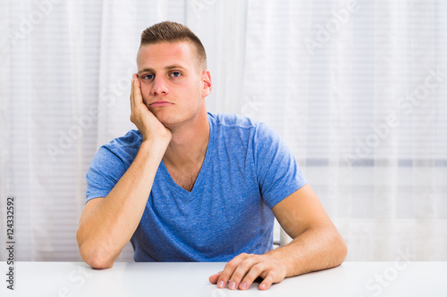 Depressed young man is sitting at the table and thinking about something. © inesbazdar