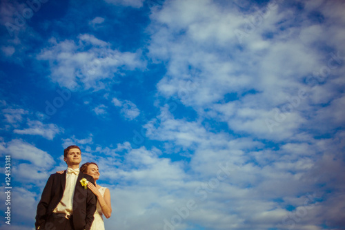 Bride daydreams leaning to groom's shoulder under blue sky