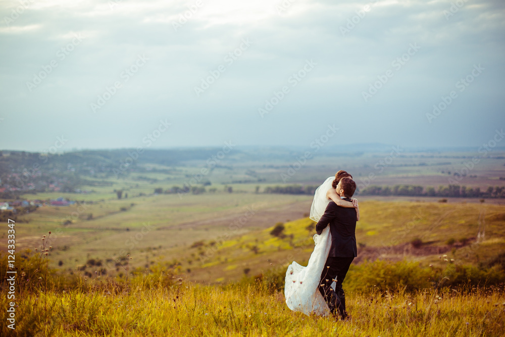 Groom raises a beautiful bride up in the air while standing on t