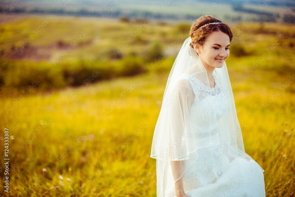 Curly bride looks on the grass while walking around the yellow f